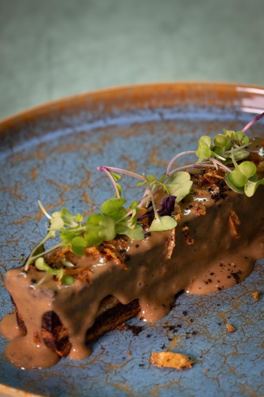 Brownie de buey napado en salsa de Oporto, con cebolla crujiente y brotes, en plato de cerámica azul