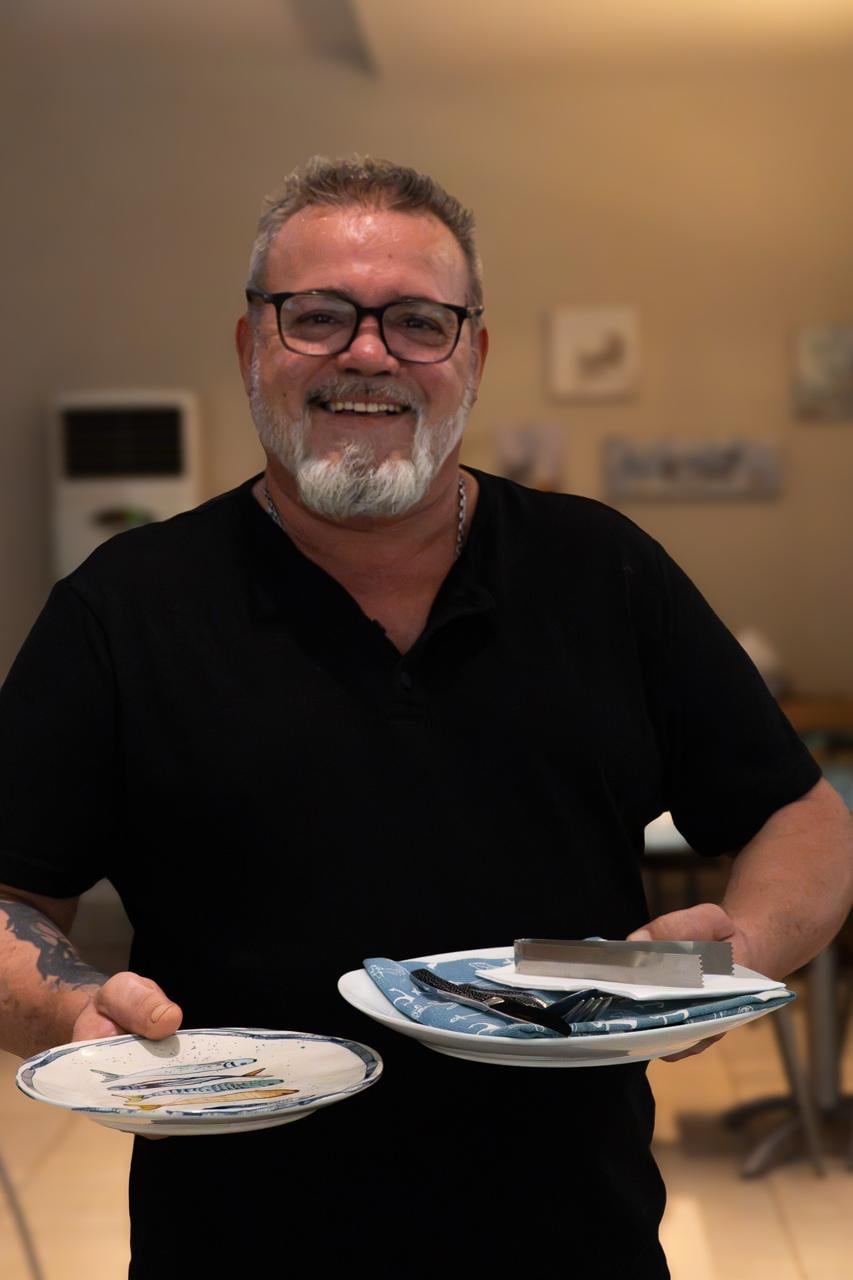 Pedro, maître de El Racó de Huelva, en la sala, sonriendo con dos platos en las manos