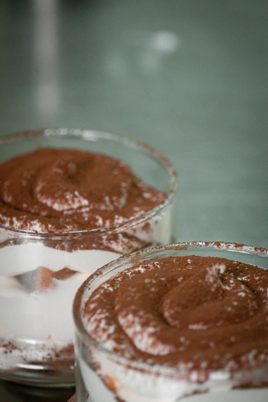 Dos vasos de tiramisú casero cubiertos de cacao en polvo